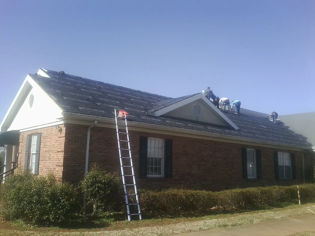 Crew tearing shingles off a brick ranch roof with a ladder set — Emergency Roof Repair work by our crew in Weeping Water
