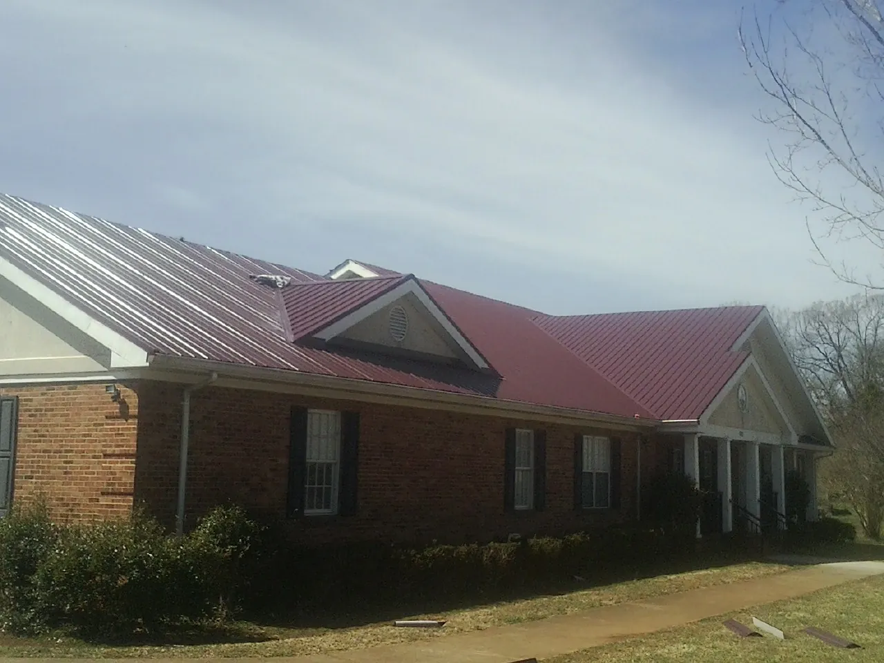Red metal roof with gabled entries on a long brick building, from a Hail Damage Roof Repair job in Weeping Water