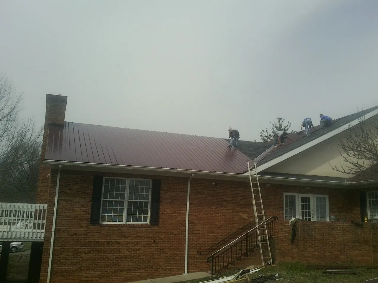 Crew setting red metal roofing panels on a brick home in Weeping Water