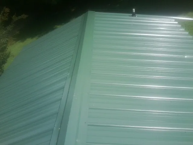New green metal panels meeting at the ridge of a roof — Flat Roof Repair work by our crew in Weeping Water