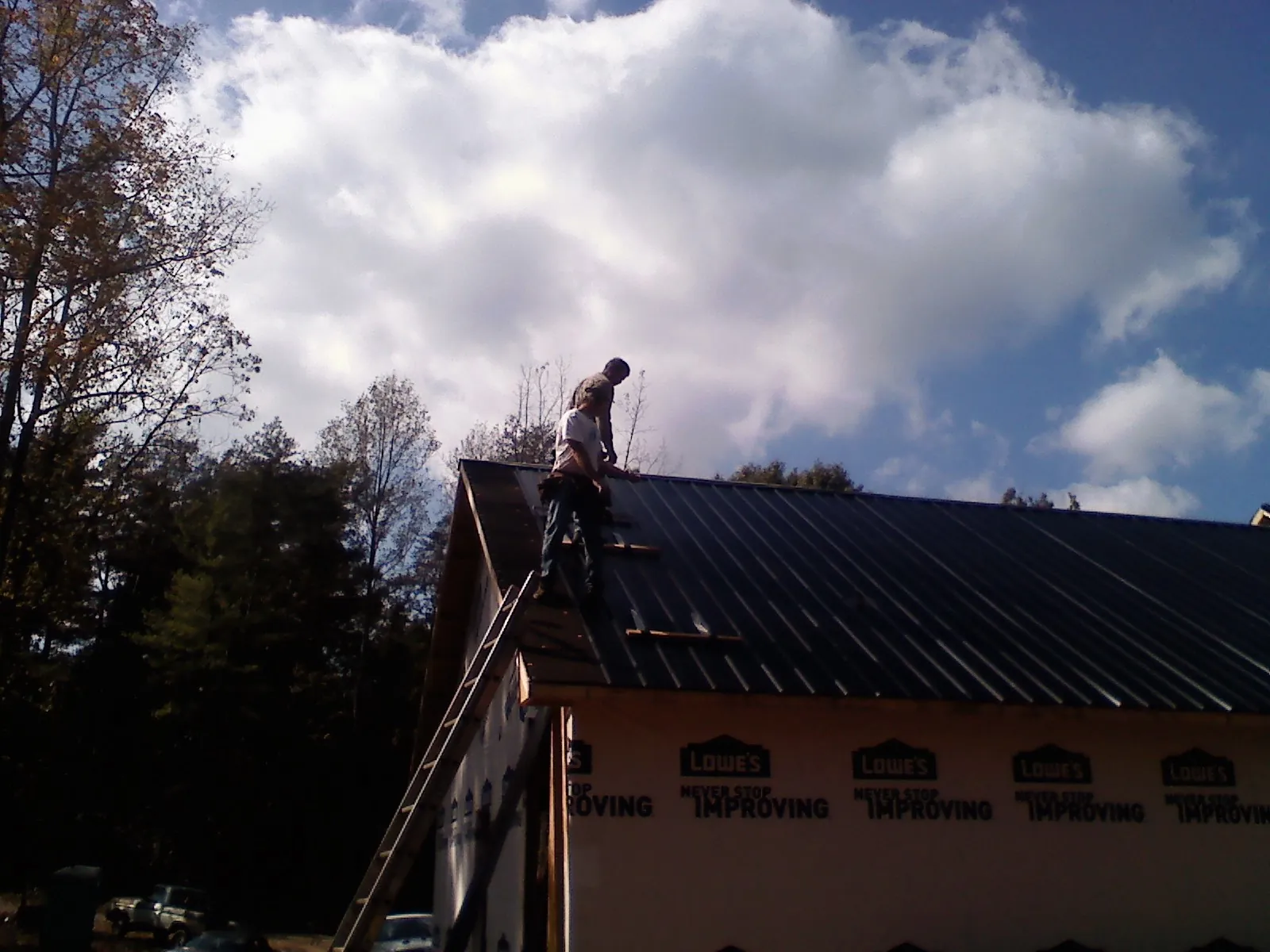 Roofer fastening dark metal panels high against a cloudy sky, from a Roof Inspection job in Weeping Water