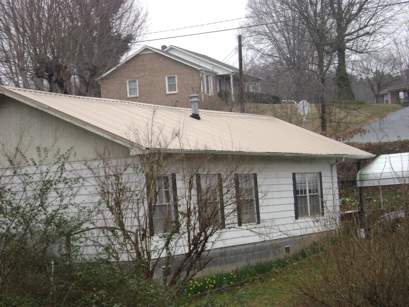 Tan metal roof on a white sided house set into a hillside — Commercial Roofing by Roofing Brothers in Weeping Water